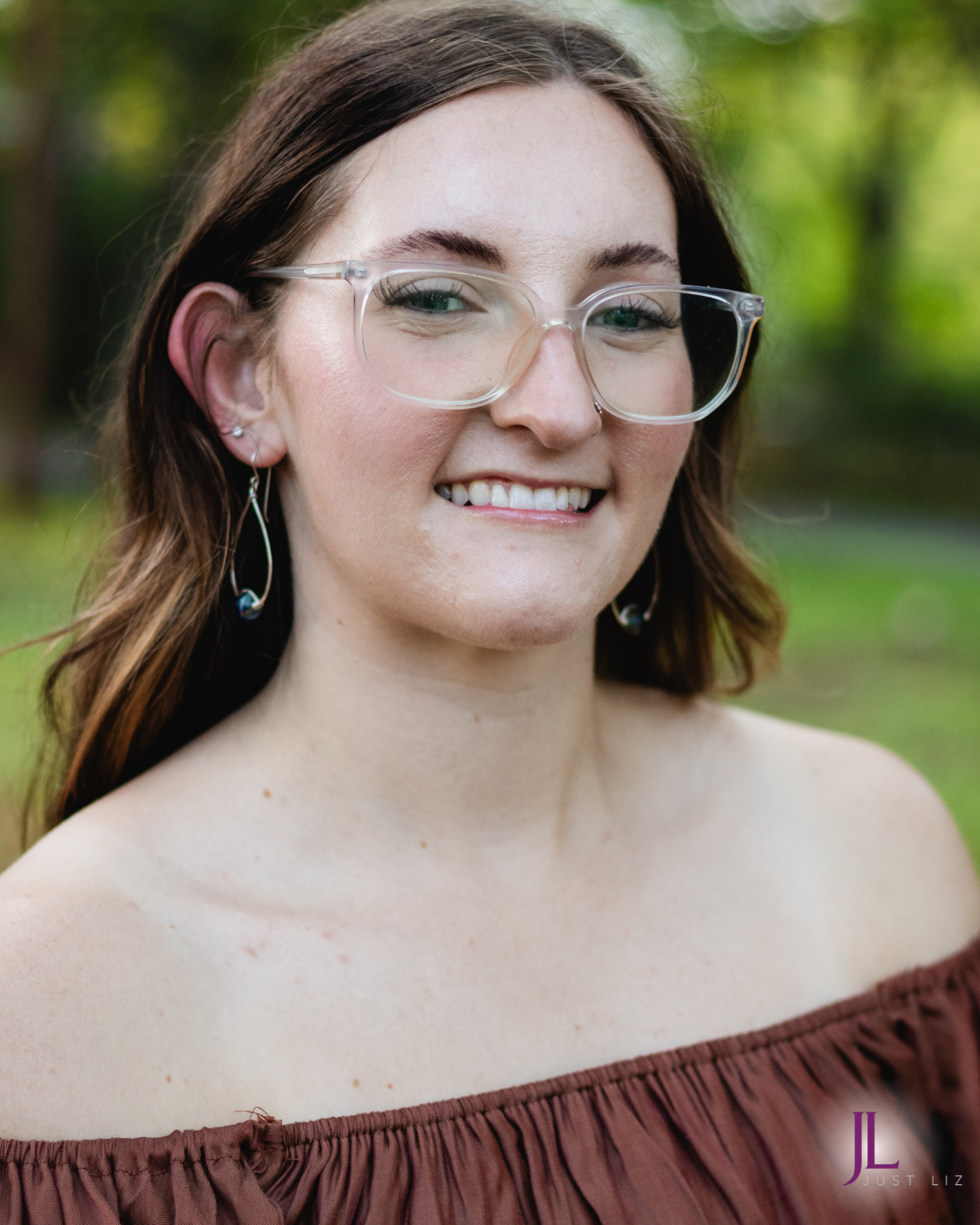 Woman smiling and wearing silver tear dropped hoop earrings with a blue glass bead at the bottom