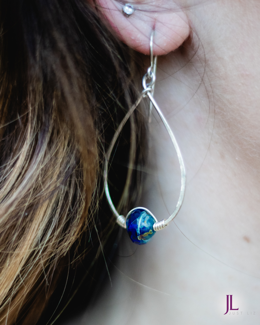 Woman wearing a silver tear dropped hoop earring with a blue glass bead at the bottom