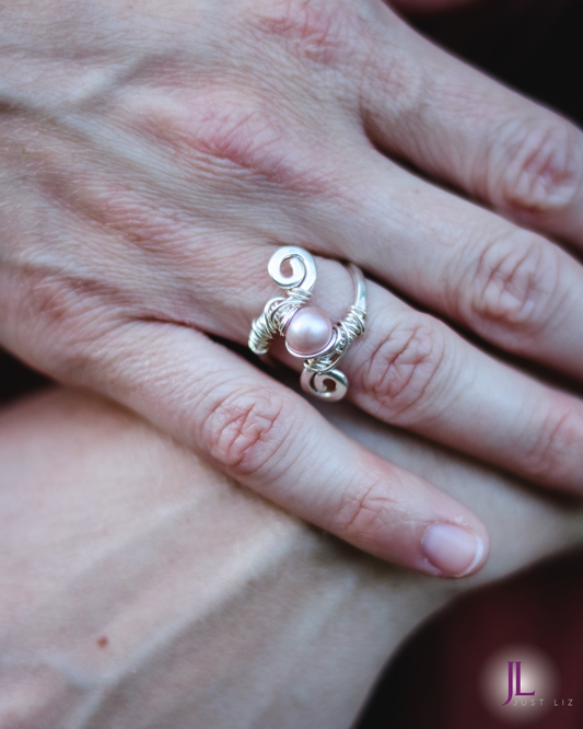 Woman wearing a silver wire wrapped swirly ring with a pink pearl in the middle