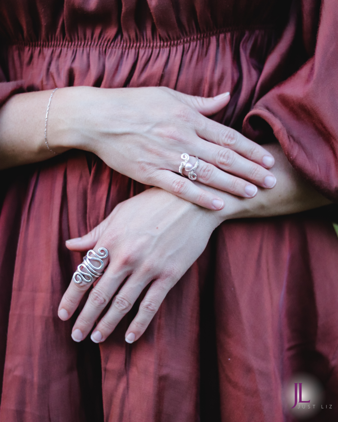 Woman wearing a swirly silver long ring and a silver wire wrapped swirly ring with a pink pearl in the middle ring