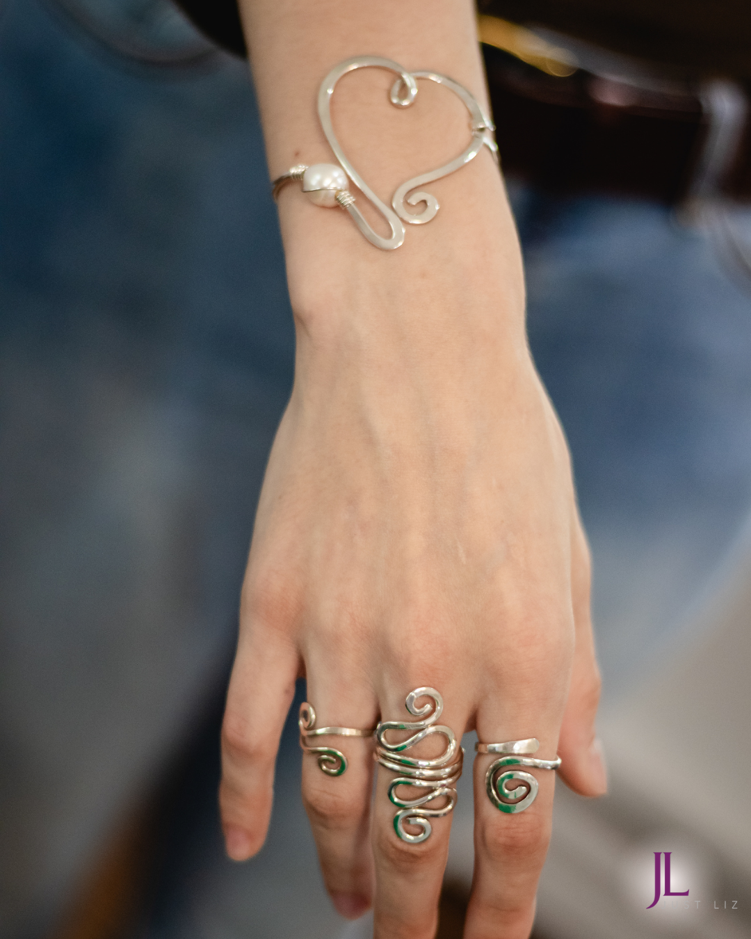 Woman wearing a swirly silver rings and silver heart bracelet with a pearl