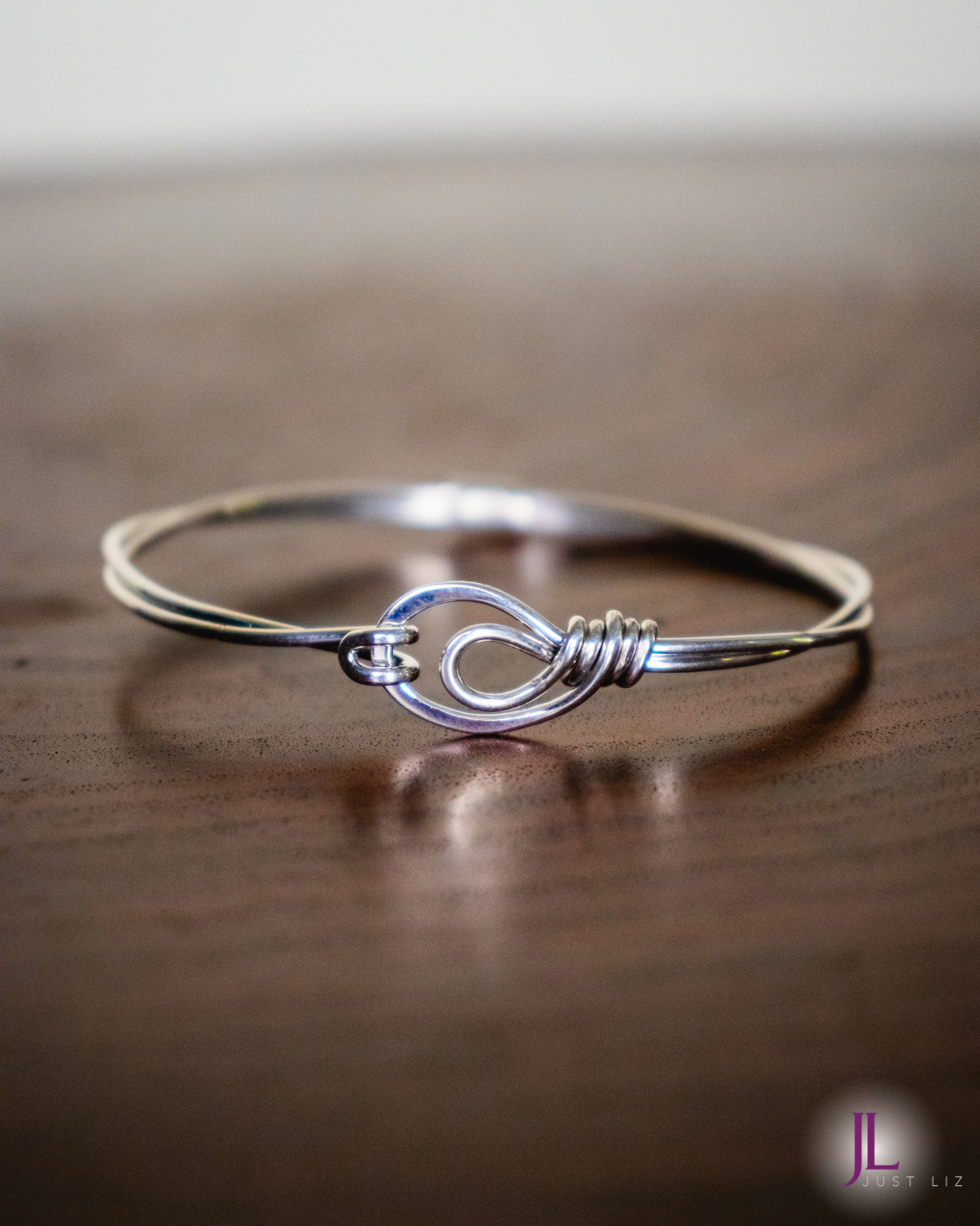 A sterling silver wire wrapped bracelet with a looped clasp opening on a table