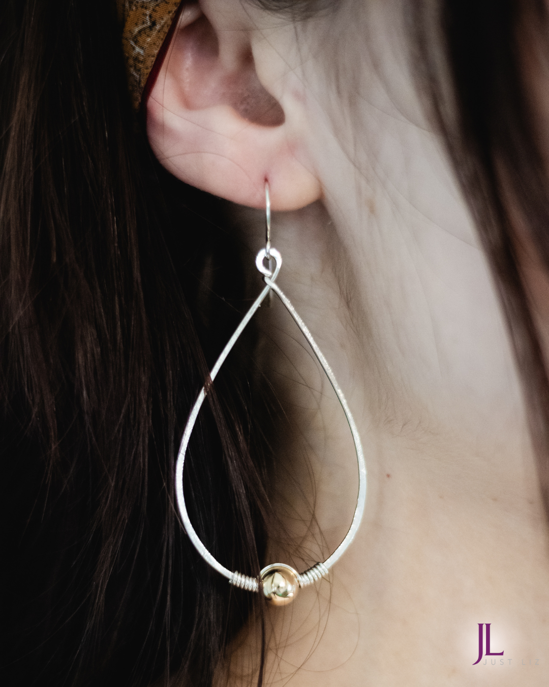 Woman wearing a silver teardrop hoop earring with a gold bead at the bottom