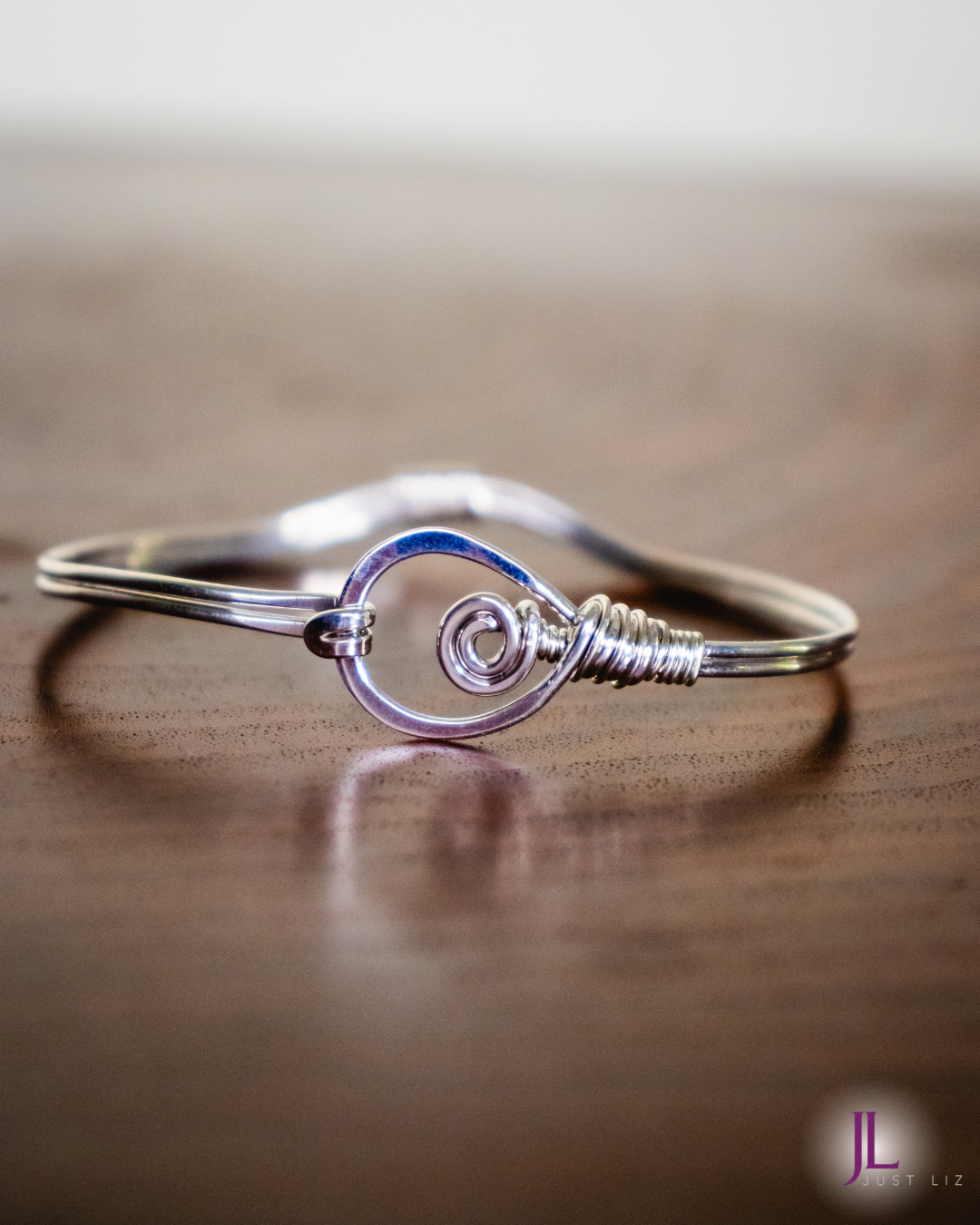 A sterling silver wire wrapped bracelet with a large looped clasp opening on a table