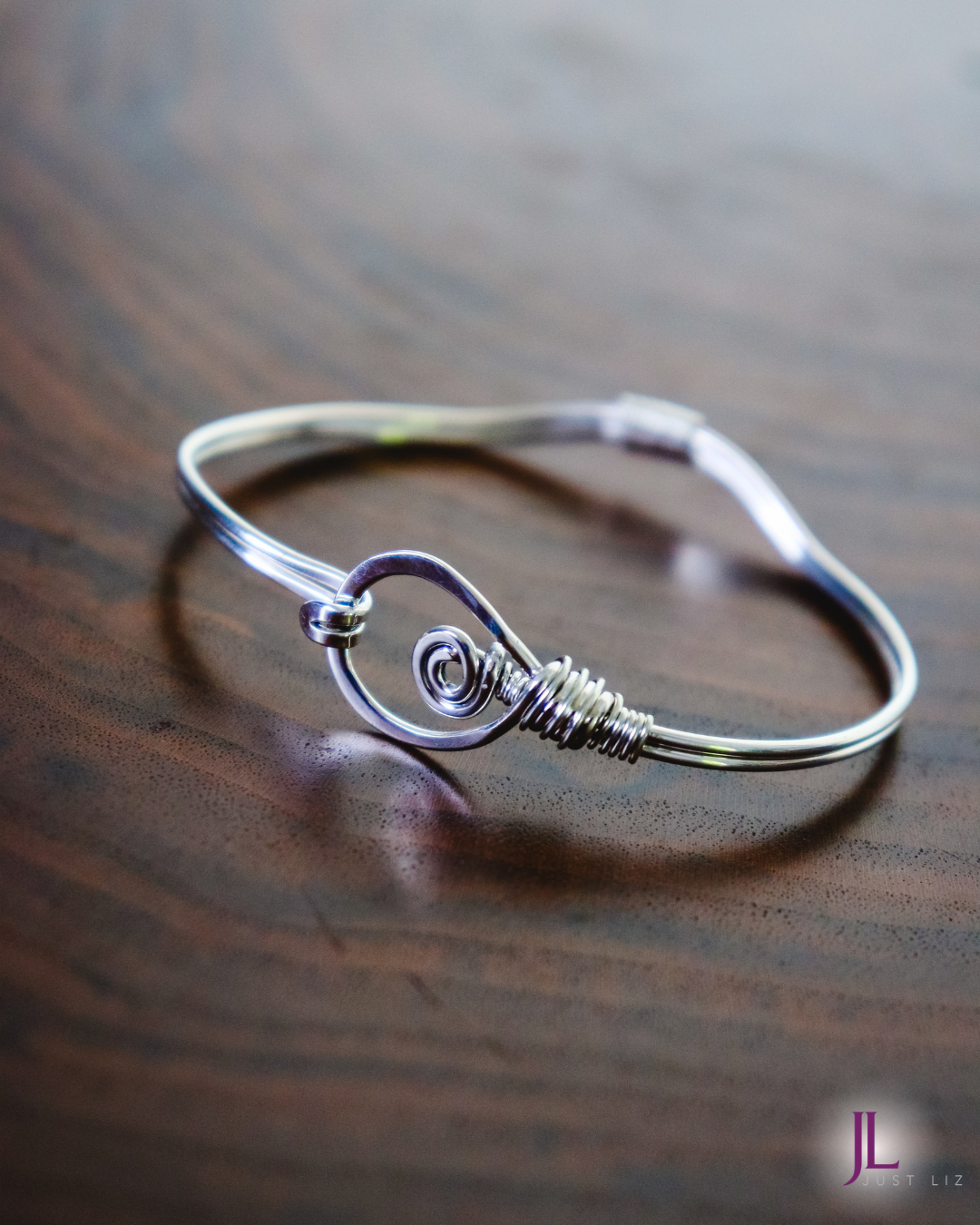 A sterling silver wire wrapped bracelet with a large looped clasp opening on a table
