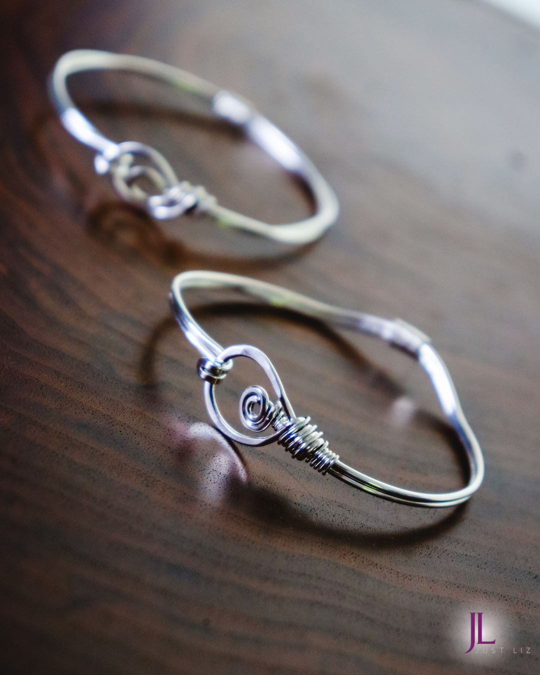 Two sterling silver wire wrapped bracelets with large looped clasp openings on a table