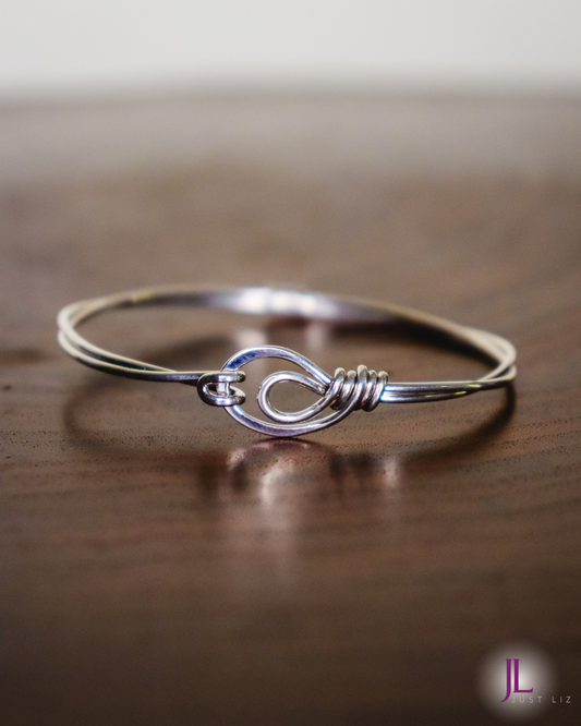 A sterling silver wire wrapped bracelet with a looped clasp opening on a table