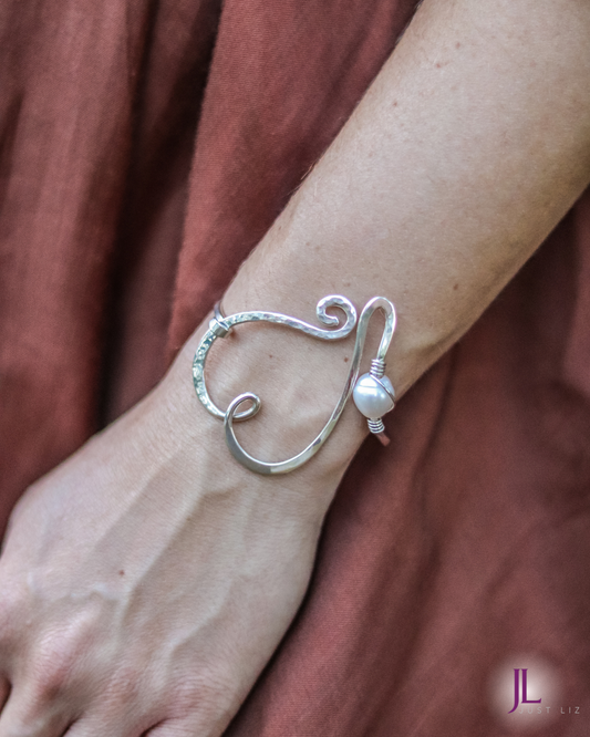 Woman wearing a swirly silver heart bracelet with a pearl